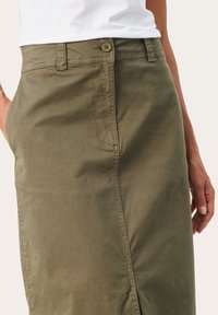 Olivgrüner Rock aus glattem Stoff, mit einem Knopfverschluss, seitlichen Taschen und einer dezenten Nahtverarbeitung an der Seite.