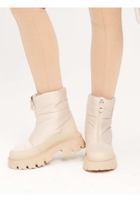 Botas de tobillo acolchadas en rosa claro con suela gruesa beige, cremallera lateral y textura suave. Diseñadas para proporcionar calor y comodidad.