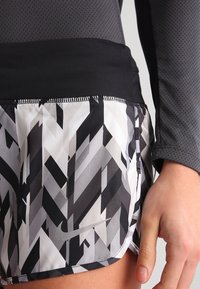 Nike idrottsshorts med svart midjeband och mönstrad grå och vit tyg med zigzag-mönster. Materialet ser slätt och lätt ut.