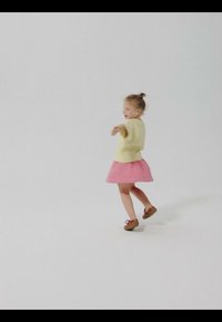 Ung pige i gul top og rosa nederdel, der snurrer med udstrakte arme mod en ensartet lys baggrund.