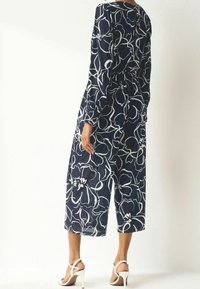 Combinaison bleu marine avec motif floral blanc, dotée de manches longues et d'une taille cintrée, jambières larges raccourcies et tissu texturé.