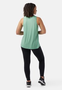 Top sin mangas verde hecho de tela suave, combinado con leggings negros y zapatillas deportivas negras. El top tiene un dobladillo curvado y un ajuste relajado.