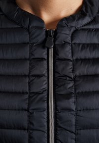 Black puffer jacket with a zippered front, featuring a textured quilted design and a soft, smooth fabric. Silver zipper hardware visible.