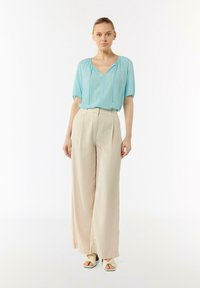 Light blue blouse with a V-neck and short sleeves paired with wide-leg beige trousers and cream sandals, featuring a textured fabric.