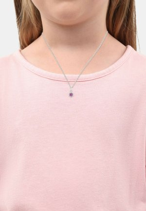 Collana in argento con un pendente floreale che presenta una gemma rosa, indossata su una camicia rosa chiaro con maniche corte.