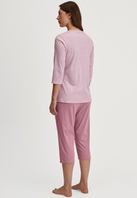 Lichtroze top met driekwartmouwen, subtiele strepen en een relaxte pasvorm, gecombineerd met bijpassende cropped broek, beide gemaakt van zachte stof.