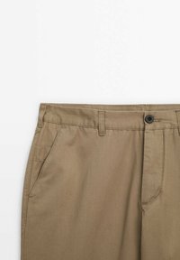 Pantalon de couleur kaki avec passants pour ceinture, fermeture à bouton noir, poches latérales et un design avant épuré sur fond blanc.
