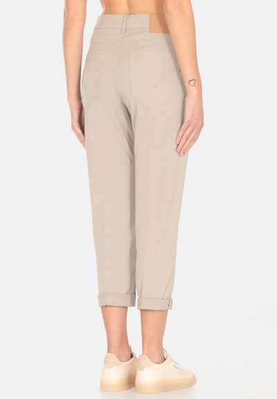 Pantaloni beige a vita alta con risvolti, due tasche posteriori e una texture liscia. Abbinati a sneaker di colore chiaro.