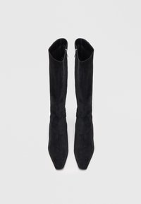Botas pretas acima do joelho feitas de camurça suave, com um bico apontado e uma forma estreita e ajustada, com um fecho de correr no lado interno.