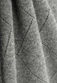 Tissu en laine grise avec un motif en diamant texturé et des fibres visibles, mettant en avant une apparence douce et chaleureuse.