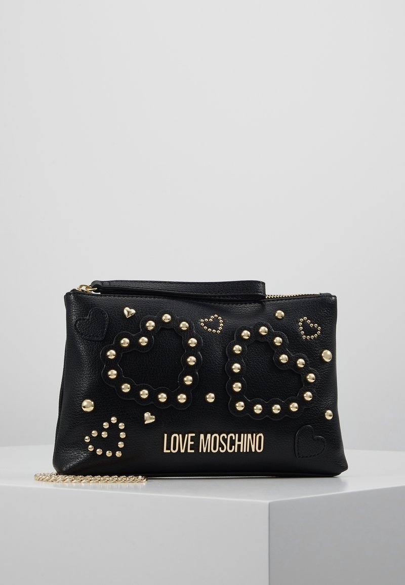 Černá kožená klutch s zlatými hroty. Obsahuje vzory srdcí a zlaté logo. Zapínání na zip a odnímatelný řetízkový popruh. Texturovaný povrch.