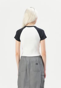 T-shirt med raglanärmar, vit kropp och svarta ärmar. Texturerat tyg, figursydd design. Bärs med en grå kjol med sidfickor.