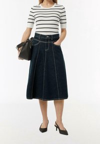 Džínová sukně s volánkovým designem, tmavě modré barvy, s kontrastním bílým prošíváním a předními kapsami; v kombinaci s pruhovaným topem a černou taškou.