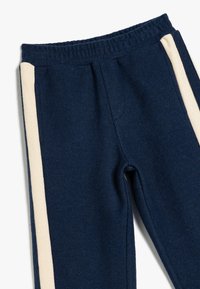 Donkerblauwe joggers van ribstof, met crèmekleurige verticale strepen aan de zijkanten en een elastische waistband voor extra comfort.
