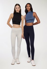 Czarne i szare crop topy z wysokim kołnierzem zestawione z szarymi i granatowymi legginsami; wszystkie ubrania są dopasowane i wykonane z gładkiego materiału. Białe sneakersy.