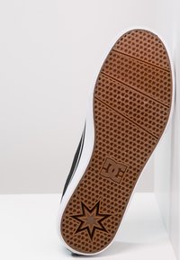 Black skate shoe outsole with a textured pattern, featuring a brown rubber base and white edging. Notable star design and DC logo.