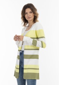 Cárdigan a rayas en blanco, amarillo y verde oliva. Tejido suave, mangas largas, frente abierto y cae por debajo de las caderas. Combinado con vaqueros.