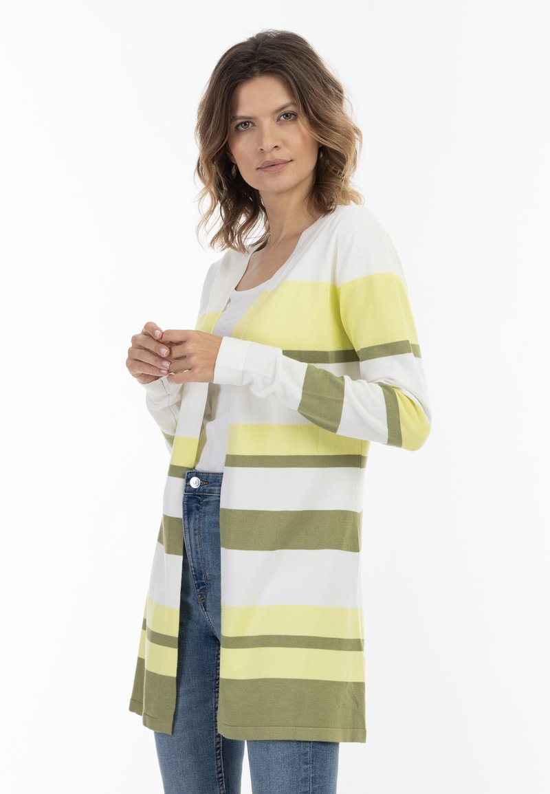 Cárdigan a rayas en blanco, amarillo y verde oliva. Tejido suave, mangas largas, frente abierto y cae por debajo de las caderas. Combinado con vaqueros.