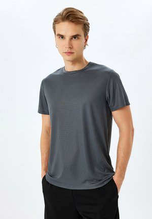 Camiseta de manga corta gris con canalé y cuello redondo, con una textura suave y corte relajado, combinada con pantalones negros.