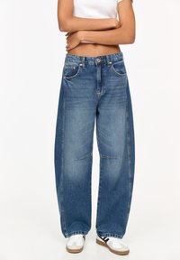 Jeans largi de culoare albastră, din denim, cu talie înaltă, două buzunare frontale și închidere cu nasture, având o nuanță deschisă și o ușoară decolorare.