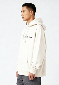 Felpa con cappuccio beige chiaro con tasca a marsupio, cappuccio con coulisse e testo ricamato nero "Non mi interessa" sul davanti. Materiale in misto cotone.