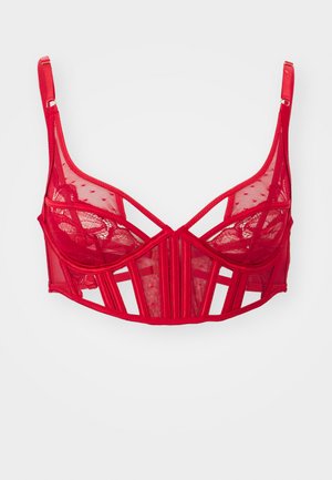 Červená krajková podprsenka s průhledným designem, geometrickými výřezy, nastavitelnými ramínky a kombinací hladkých a texturovaných panelů.