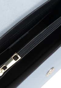 Innenraum der hellblauen Geldbörse mit einer schwarzen Reißverschlusstasche, glatter Textur, goldenen Beschlägen und einem Druckknopfverschluss.