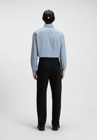 Camicia a maniche lunghe azzurro chiaro con bottoni abbinata a pantaloni neri. La camicia presenta un colletto classico e dettagli di cucitura visibili.