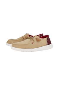 Scarpe in tela beige con superficie texturizzata, suola in gomma bianca e dettagli color bordeaux sul colletto. Presentano lacci marroni e cuciture decorative.