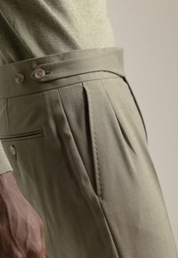 Pantalones verde oliva con un corte ajustado, que presentan un cierre de doble botón, pliegues laterales y una textura de tela fina.