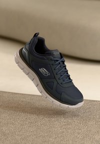 Dark blue sneaker with mesh and synthetic material. Features lace-up design, rounded toe, padded collar, and white rubber sole.