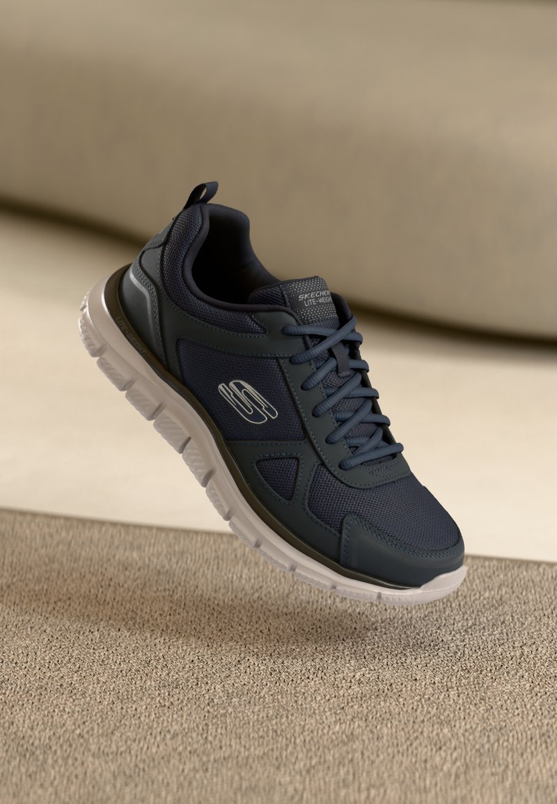 Dark blue sneaker with mesh and synthetic material. Features lace-up design, rounded toe, padded collar, and white rubber sole.