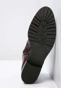 Zapato de cuero burdeos con suela de goma negra texturizada que presenta un diseño de relieve. Acento de cremallera lateral para facilitar el uso. Marca Gabor visible.