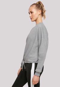 Lichtgrijze sweatshirt met geribde manchetten en een trekkoord onderaan, gedragen met zwarte broeken met witte zijstrepen. Gladde stof, casual pasvorm.
