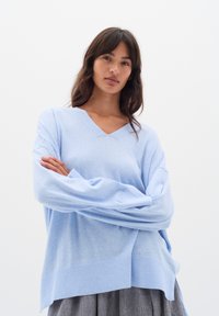 Hellblauer, lässig sitzender Pullover mit V-Ausschnitt, langen Ärmeln und geripptem Saum. Weicher Stoff, lässiges Design, minimalistischer Stil.