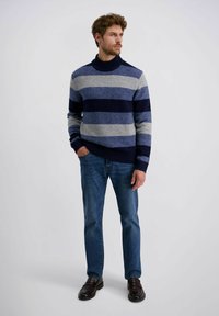 Blauw en grijs gestreepte trui met een hoge ribbels boord, gecombineerd met blauwe jeans en donkere instappers, gemaakt van textuurstof.