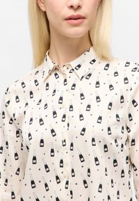 Knap-up skjorte lavet af let stof, med et champagneflaske mønster i sort, hvid og blå stjerner på en beige baggrund.