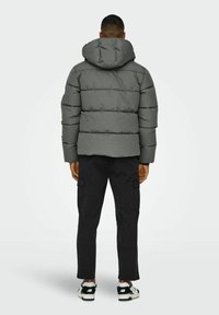 Gray puffer jacket with a hood, featuring horizontal stitching and a relaxed fit. Worn over black cargo pants and sneakers.