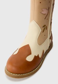 Brown and cream leather ankle boot with floral cutout designs, rounded toe, and stitched accents along the sole. Textured surface.