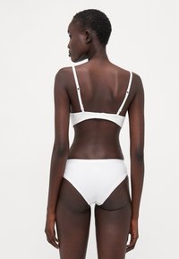 Vitt bikini-set med en enkel design, justerbara axelband, spänne och en mjuk tygtextur, lämpligt för badkläder.