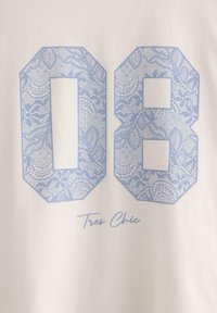 Hvidt stof med tallet "08" i et lysblåt blondermønster og teksten "Tres Chic" i kursiv nedenfor.