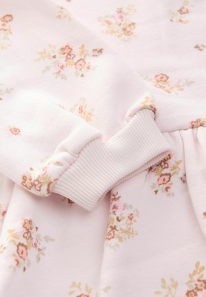 Rosa blumengemusterter Stoff mit gerippten Bündchen. Enthält kleine Blumen in Pink- und Beigetönen vor einem sanften rosa Hintergrund. Glatte Textur.
