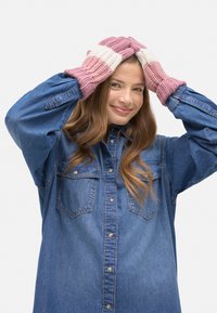 Guantes de punto con diseño de rayas rosas y blancas, con puños acanalados. La modelo lleva una camisa vaquera azul, con las manos en la cabeza.