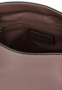 Innenansicht einer staubigen rosa Lederhandtasche mit strukturierter Oberfläche, ausgestattet mit einer Reißverschlusstasche und Gabor-Branding auf einem braunen Lederanhänger.