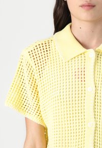 Polo shirt giallo lavorato a maglia a maniche corte con un design a rete aperta texturizzata, dotato di colletto e chiusura a bottoni.