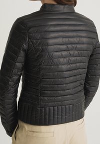 Svart vadderad jacka med horisontellt kviltad design, hög krage och ribbad nederdel. Har en slät, glänsande yta.