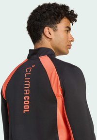Black athletic shirt with coral accents, high collar, and "CLIMACOOL" logo. Features a textured design along the sleeves and back.