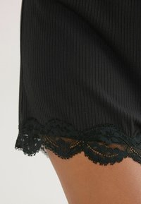Zwarte geribbelde shorts met een golvende zwarte kantafwerking aan de zoom. De textuur is glad met een lichte glans, die het kantdetail benadrukt.