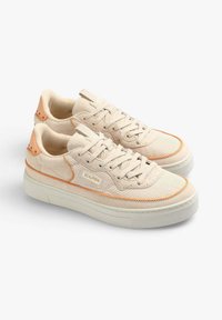 Baskets beiges avec un tissu texturé, des accents orange et une épaisse semelle blanche. Présentent des lacets ronds et des œillets en métal. Logo de la marque visible.