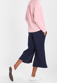 Ljusrosa långärmad skjorta med veck bak, i kombination med navy culotter och vita sneakers, som har en avslappnad siluett.